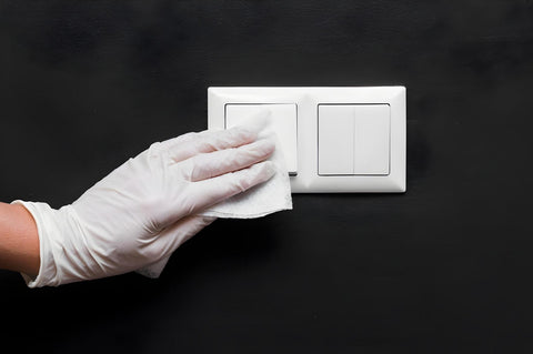 Gloved hand wiping a light switch plate